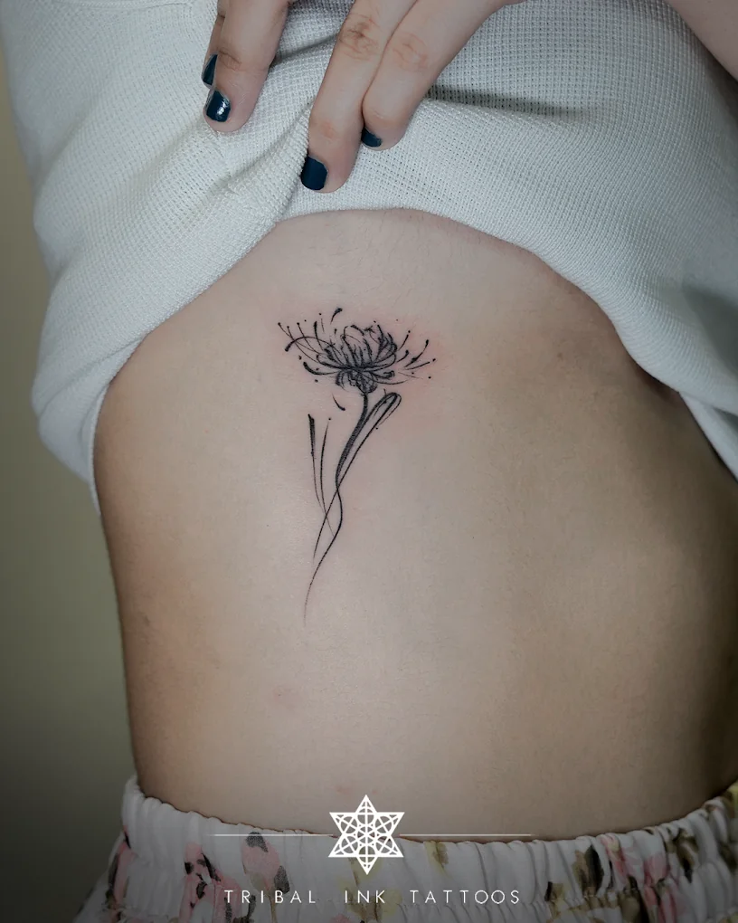 A chrysanthemum drawn in single-needle fine line on a woman's ribs.
